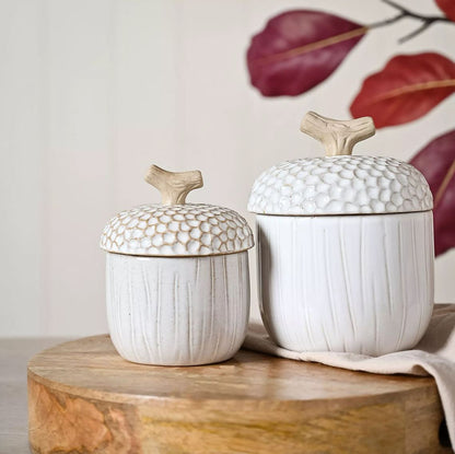 Two white ceramic jars with textured lids on a wooden surface.