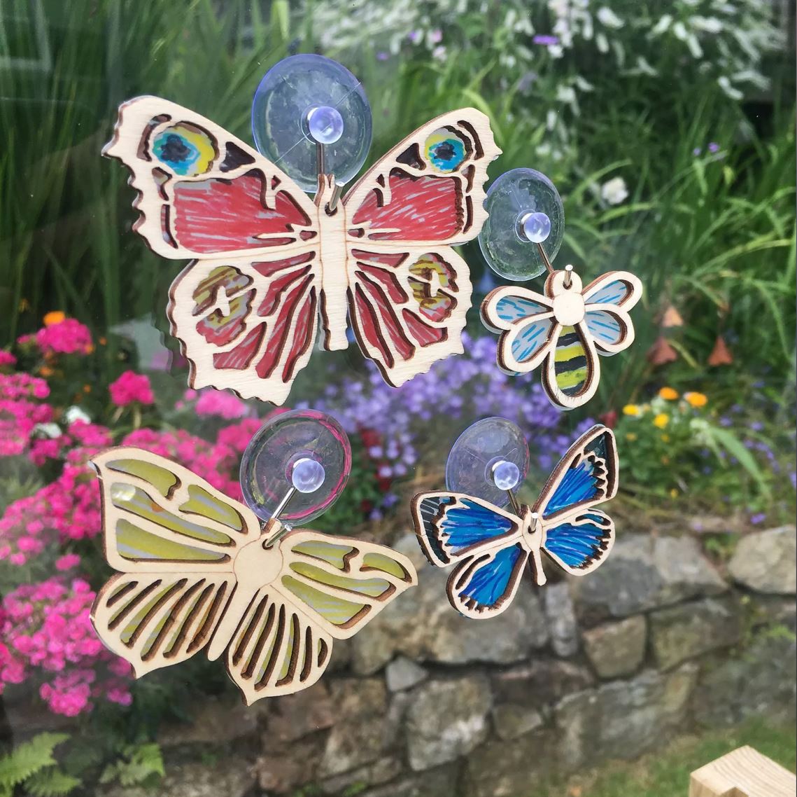 Apples To Pears Gift In A Tin Butterflies & Bees Suncatcher Kit stuck on window in front of garden