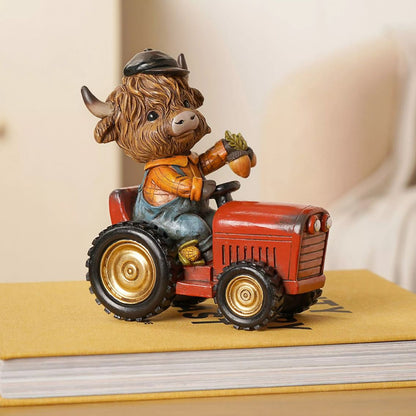 A decorative figurine of a Highland cow driving a small red tractor, placed on top of a yellow book with a softly blurred indoor background.