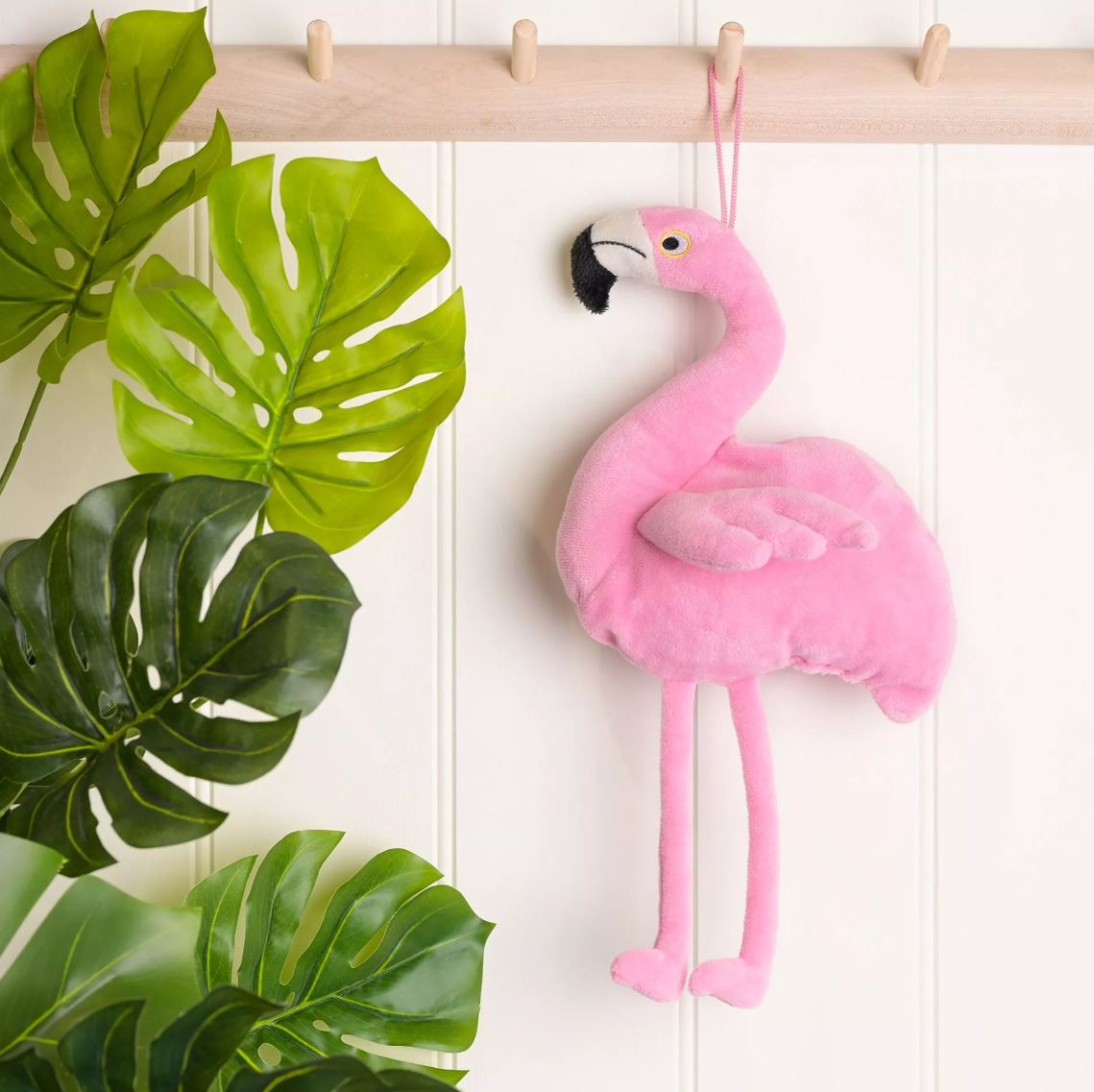 Flamingo hung up on a coat peg with leaves to the side
