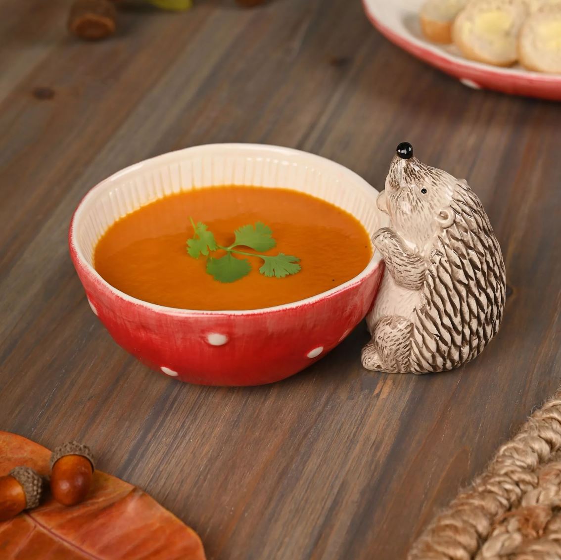 Red bowl of soup with a decorative hedgehog on a wooden surface