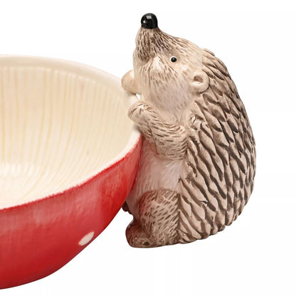 A ceramic hedgehog-shaped bowl holder next to a red and cream-colored ceramic bowl, shown on a plain white background.