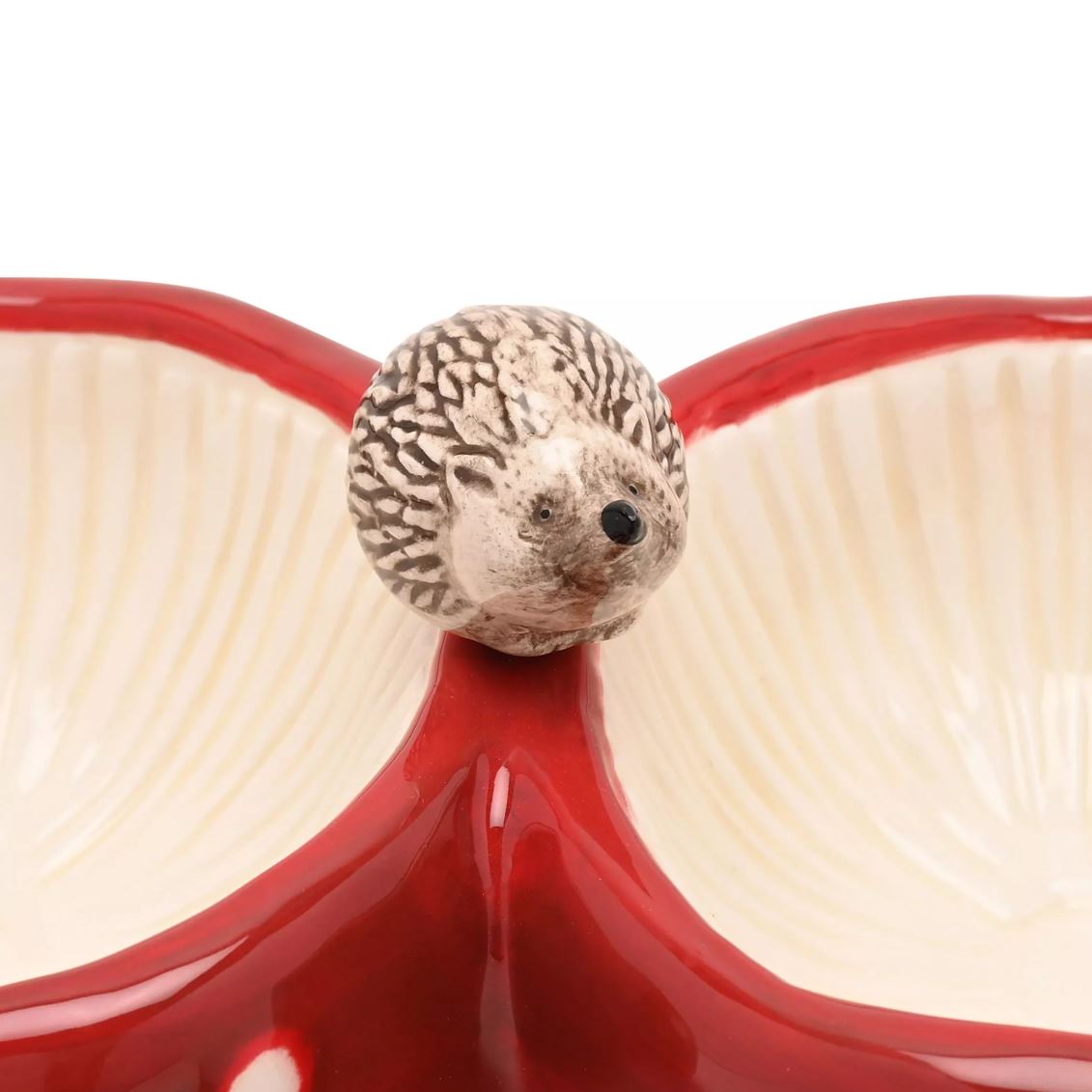 A ceramic hedgehog figurine perched on the center divider of a red and cream split platter, photographed against a plain white background.