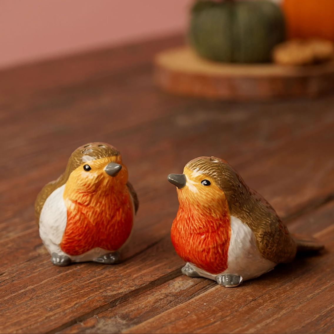 Two small robin bird figurines with orange-red bellies, brown backs, and white underbellies sitting on a wooden surface with a softly blurred background.