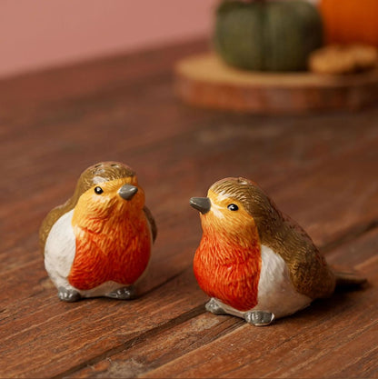 Two small robin bird figurines with orange-red bellies, brown backs, and white underbellies sitting on a wooden surface with a softly blurred background.