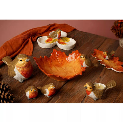 A set of autumn-themed ceramic tableware displayed on a dark wooden table, including a large leaf-shaped bowl, bird-shaped candle holders, and small dish pieces.