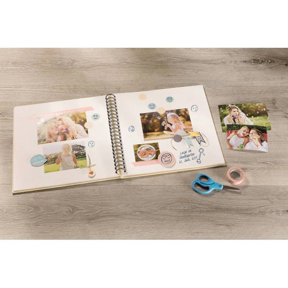 Open photo album with printed photos on a wooden surface, accompanied by scissors and tape.