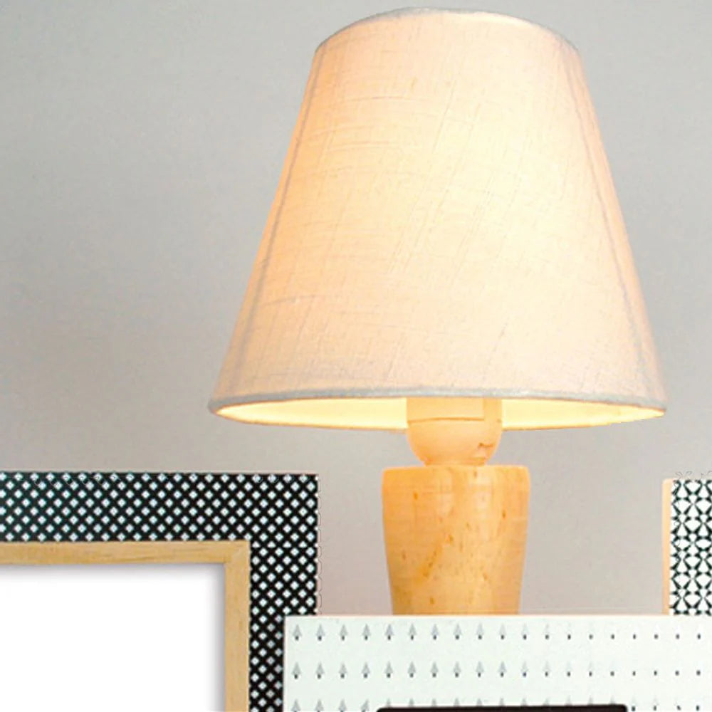 Table lamp with a beige shade on a surface with decorative frames in the background.