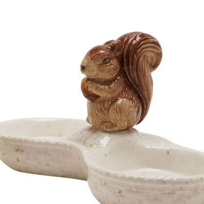 A ceramic squirrel figurine in brown glaze sitting on top of a cream-colored bone-shaped dish with speckled texture, isolated on a white background.