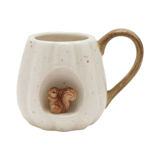 A ceramic mug shaped like a cream-colored pumpkin with brown speckles, featuring a carved-out center containing a small brown squirrel figurine and a matching brown handle.