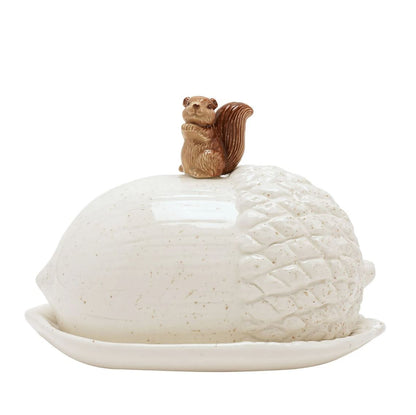A ceramic butter dish shaped like a nut, with a textured off-white body, a matching lid, and a small brown squirrel figurine on top, set against a plain white background.