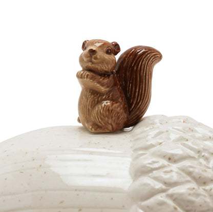 A small glazed ceramic squirrel figurine in brown tones, perched on top of a textured off-white ceramic lid against a plain white background.