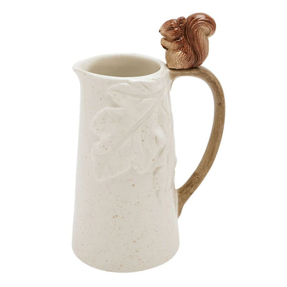 A speckled cream-colored ceramic pitcher with embossed leaf details, a brown handle, and a small brown squirrel figurine on top of the handle, shown against a plain white background.