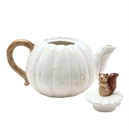 A white ceramic pumpkin-shaped teapot with a ribbed texture, speckled finish, and a rustic brown handle, shown alongside a matching lid topped with a small brown squirrel figurine, on a white background.