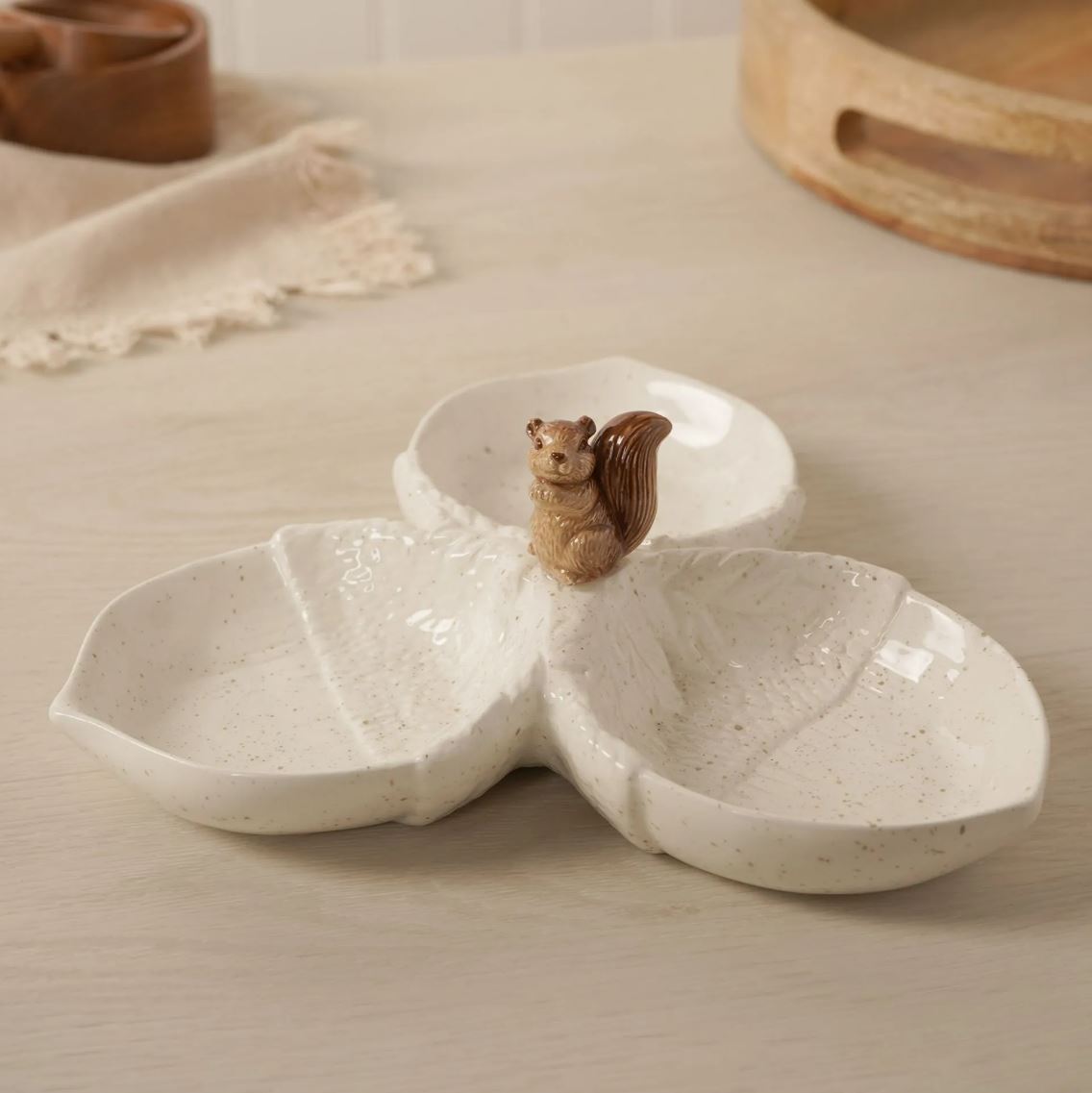 A three-compartment ceramic tray with a small brown squirrel figurine on the top center, displayed on a light wood tabletop.