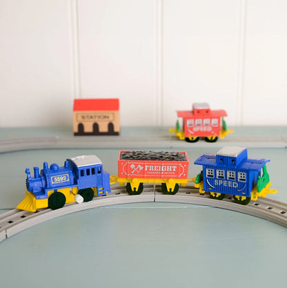 Colorful toy train set on a track with a station building in the background.